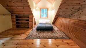 A loft bedroom with a sloped ceiling, wooden walls, a bed with pillows, a rug, and a window.