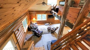 A log cabin interior with a loft bedroom, a fireplace, and a dining area.