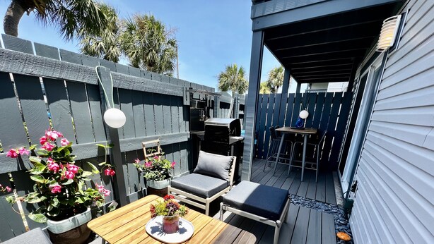 Une terrasse avec une table en bois, deux chaises, une petite table et un barbecue.