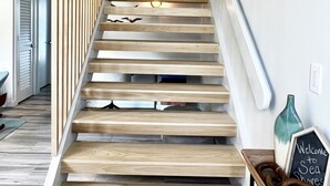 Un escalier moderne avec des marches en bois et une rampe en verre, menant à une pièce où se trouvent un tableau et un panneau noir.