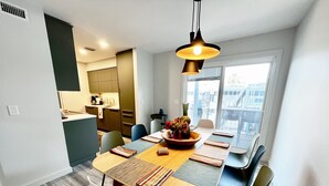 Un espace repas moderne avec une table en bois, des chaises noires et blanches, et un luminaire suspendu.