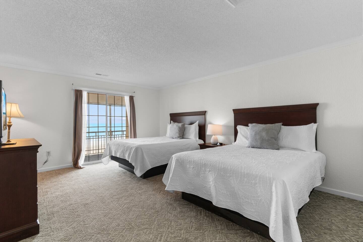Une chambre d’hôtel avec deux lits, une télévision et une vue sur l’océan, accessible par une porte coulissante.