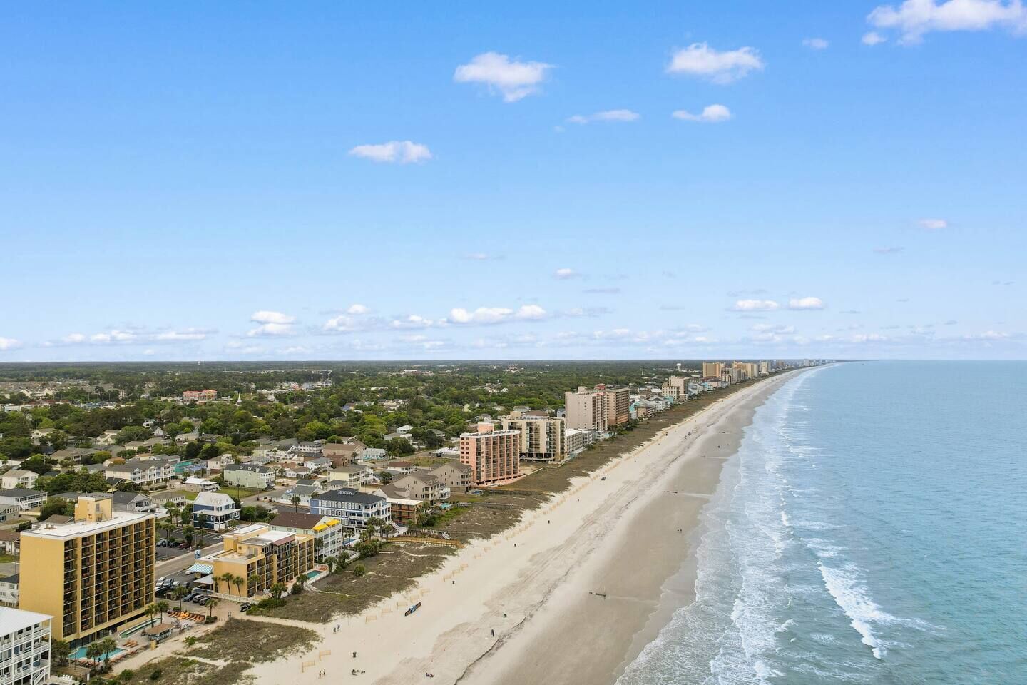 A coastal cityscape with a long beachfront, high-rise buildings, and a clear sky.