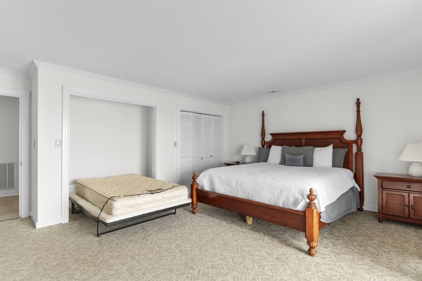 Un dormitorio con cama con dosel, una mesita de noche con lámpara y un colchón en el suelo.