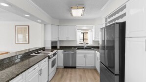A modern kitchen with white cabinetry, a stainless steel refrigerator, and a granite countertop.