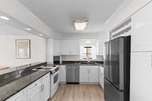A modern kitchen with white cabinetry, a stainless steel refrigerator, and a granite countertop.