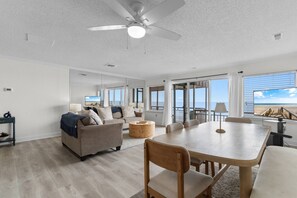 A spacious living area with a ceiling fan, a sofa, a coffee table, and a dining table with chairs. - Bright Oceanfront PH- Pools, Tiki Bar, Breakfast (North Myrtle Beach)