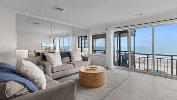 A modern living room with a sofa, coffee table, and a view of the sea through large windows.