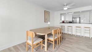 A dining area with a round table and four chairs, a ceiling fan, and a kitchen in the background.