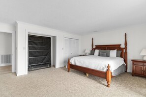Un dormitorio con cama con dosel, una mesita de noche de madera, una mesilla auxiliar, un armario y una puerta que da a otra habitación.