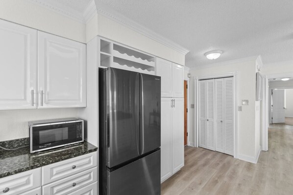Una cocina con armarios blancos, un refrigerador de acero inoxidable, un microondas y piso de madera.