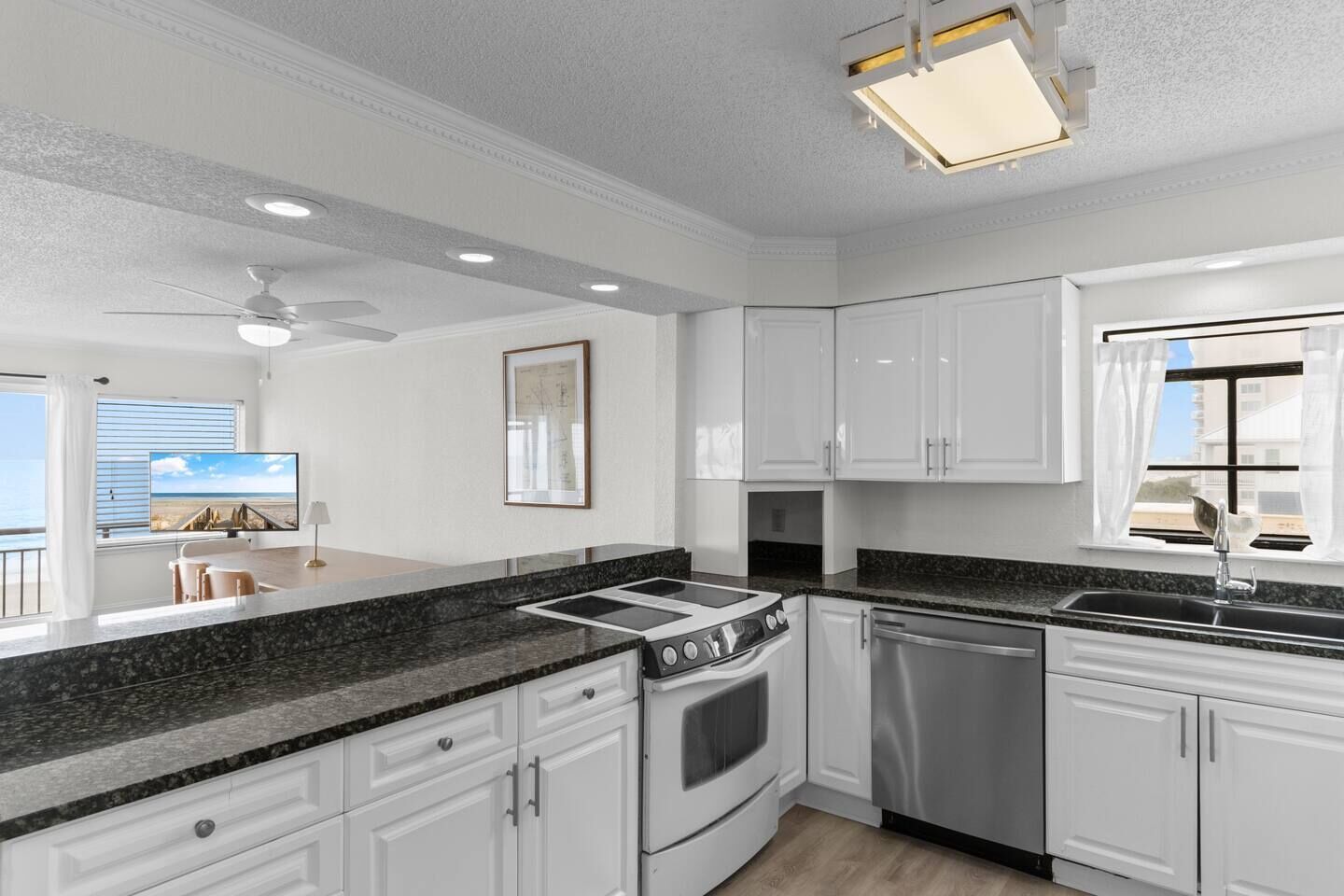 A modern kitchen with white cabinetry, a granite countertop, a built-in oven, and a dishwasher.