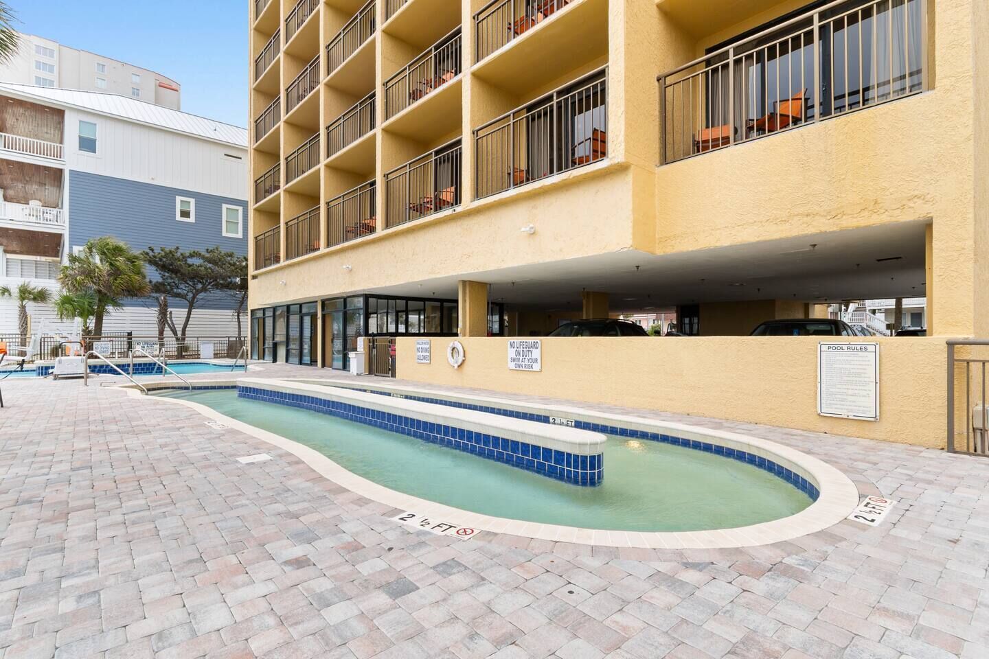 Área de piscina com deck revestido, placa indicando ausência de salva-vidas e sinalização das regras da piscina.