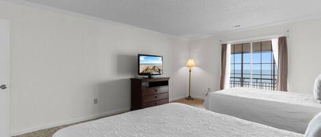 A hotel room with two beds, a television on a dresser, a lamp, and a window with a view.