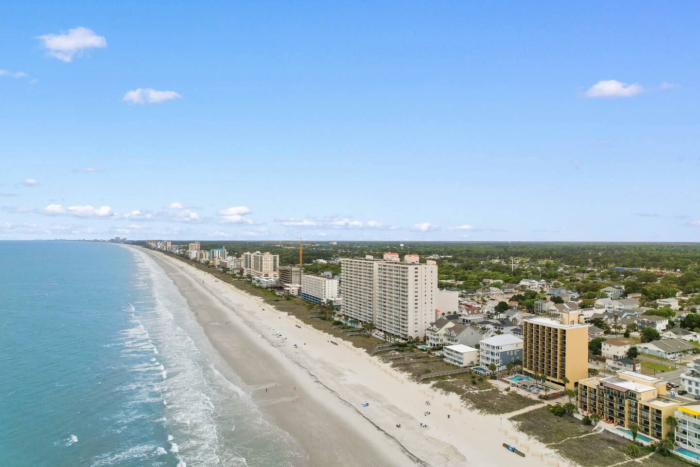 A coastal hotel with a beachfront view, multiple-story buildings, and a sandy beach.
