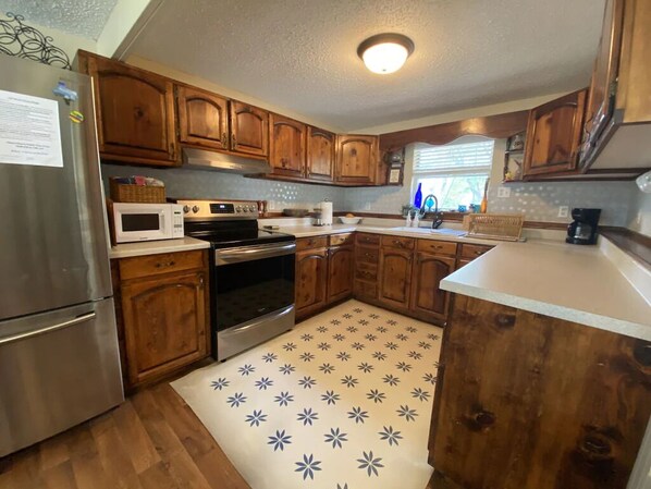 A kitchen with wooden cabinets, a stainless steel refrigerator, a microwave, an oven, and a patterned rug.