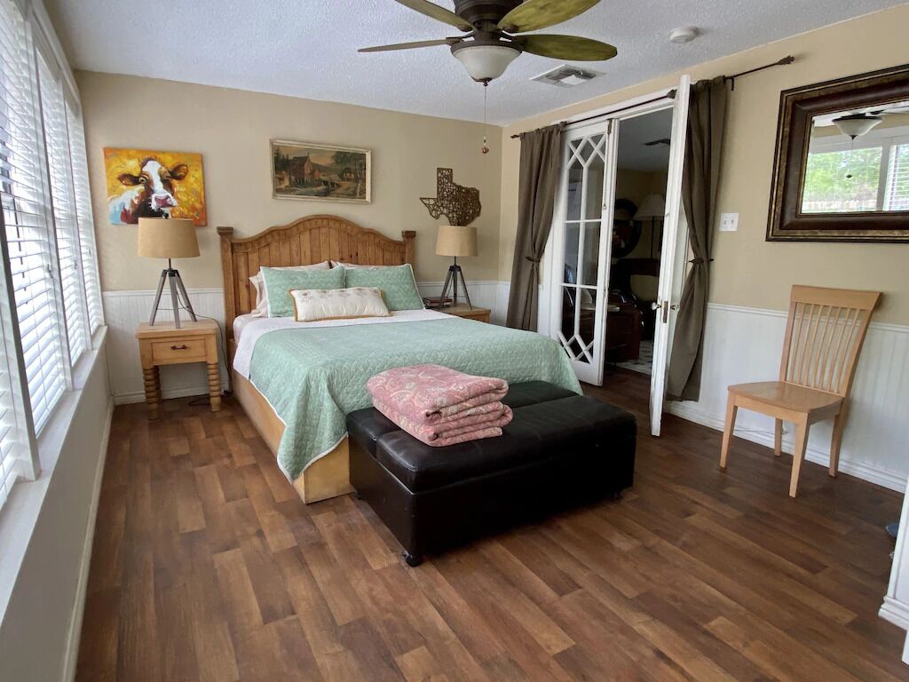 Une chambre à coucher comprenant un lit, une table de chevet, une chaise, une fenêtre et un ventilateur de plafond.