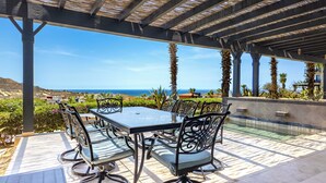 Eine Terrasse im Freien mit Tisch und Stühlen, mit Blick auf eine malerische Aussicht auf das Meer und die Hügel.