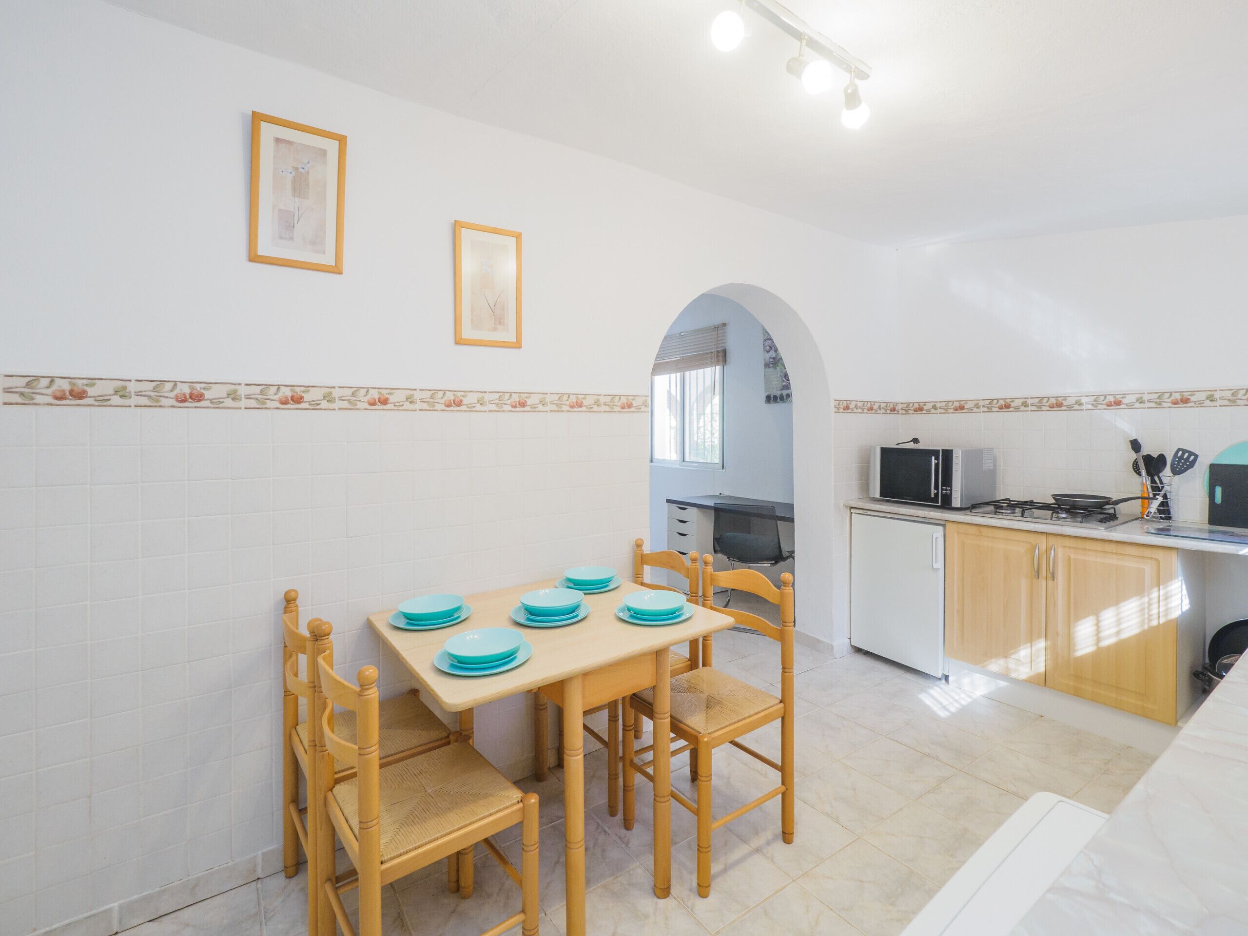 Cocina compacta con comedor, que presenta un salpicadero de azulejos, armarios de madera y una pequeña isla con microondas y estufa.