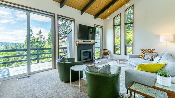 A spacious living room with a fireplace, large windows, and a balcony overlooking a forested area.
