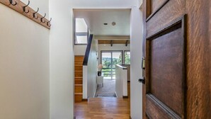 A hallway with a wooden floor, a wooden door on the right, and a staircase leading to an upper level.