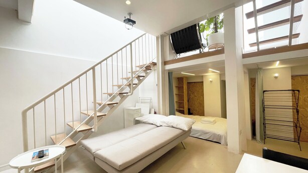 Ein kleines Schlafzimmer mit einem Einzelbett, einem kleinen Tisch, einem weißen Kleiderschrank und einer Treppe, die zu einer oberen Ebene führt.