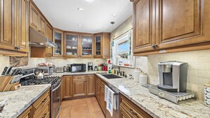 A kitchen with wooden cabinets, a stove, a microwave, and a coffee maker. - Cheerful Bedroom Beach Cottage  STR15-0264 (Dana Point)