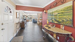 A spacious hallway with a dining area, a painting on the wall, and a wooden table with a bowl. - Cheerful Bedroom Beach Cottage  STR15-0264 (Dana Point)