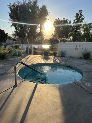 Una piscina con una escalera metálica, rodeada por una cerca blanca y una pared blanca con un letrero pequeño.