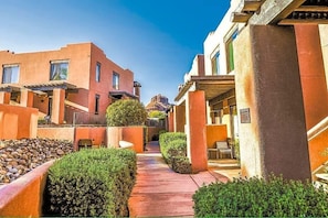 A hotel courtyard with a central pathway, surrounded by buildings with balconies and a mountain view in the background.
