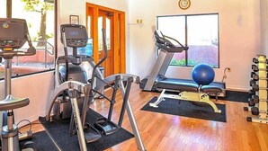 A home gym with treadmills, a stationary bike, a rowing machine, a set of dumbbells, and a large window with a view of greenery. - Sedona | Canyon Retreat | Pools, Hiking & Red Rocks (Sedona)