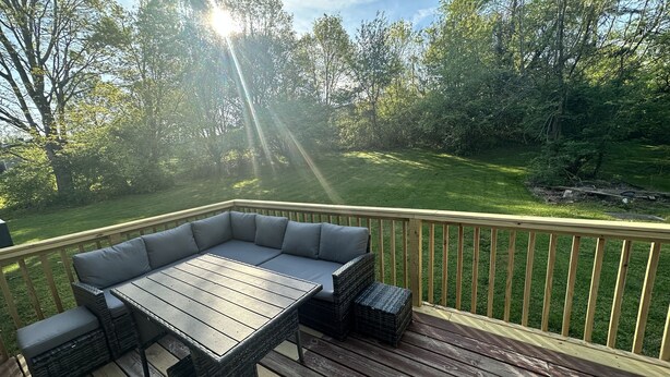 A deck with a wooden table and a cushioned seating area, surrounded by a wooden railing and a grassy yard. - family home (Knoxville)