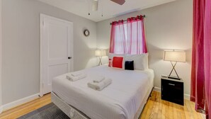 A bedroom with a bed, two bedside tables, a ceiling fan, a window with curtains, and a door.