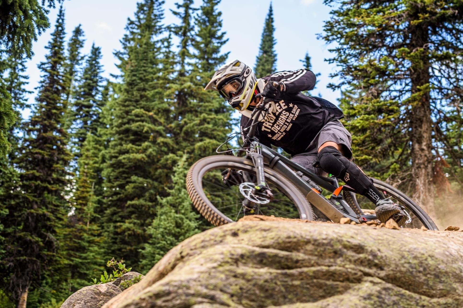 A mountain biker navigating a rocky terrain with dense forest in the background.