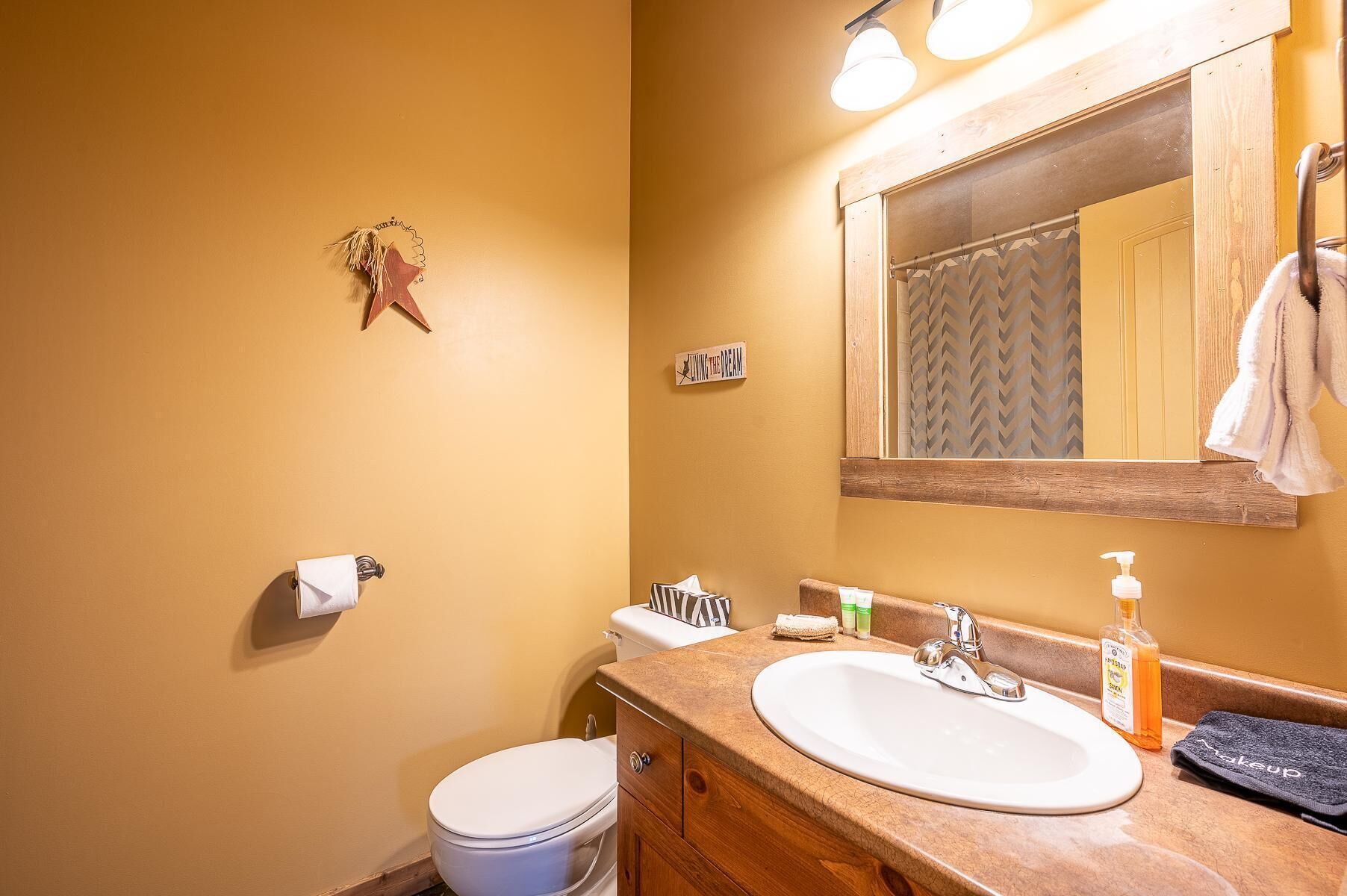 A bathroom with a white toilet, a wooden vanity with a sink, and a mirror above it.