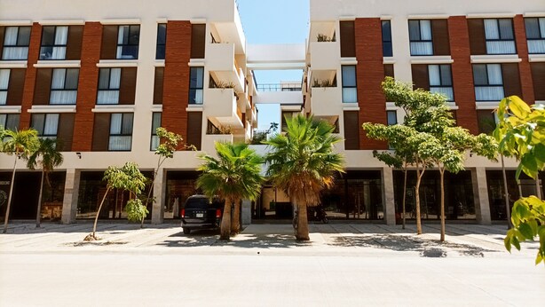 A modern building with a symmetrical facade, multiple balconies, and a central courtyard with palm trees. - VIVA 3BR 105-106 (Tulum)