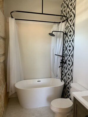 A bathroom with a freestanding bathtub, a toilet, and a shower area with a black metal rack. - The Rock Stack: Ruggedly luxurious 3 bedroom, 3 bathroom on the Llano River (Llano)