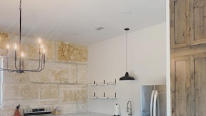 A modern kitchen with a stone wall backsplash, wooden cabinets, a stainless steel refrigerator, and a wooden dining table. - The Rock Stack: Ruggedly luxurious 3 bedroom, 3 bathroom on the Llano River (Llano)