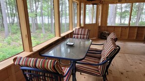 Een houten chalet met een grote eettafel en gestreepte stoelen, grote ramen en uitzicht op het bos.