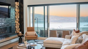 Een moderne woonkamer met een open haard, een groot raam met uitzicht op een meer en een gezellige zithoek.
