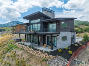 A modern two-story house with large windows, a balcony, and a stone foundation.