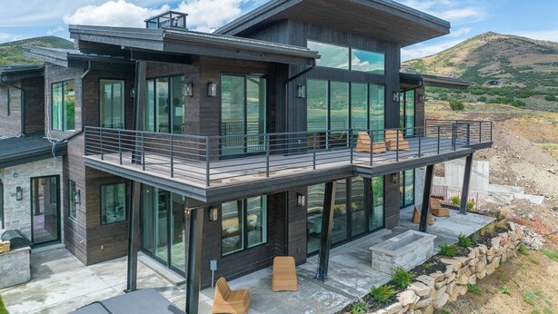Een modern huis met twee verdiepingen, grote raampartijen, een balkon met zitplaatsen en uitzicht op een glooiend landschap.