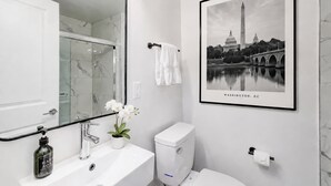 Une salle de bain avec un lavabo en marbre, des toilettes, un tableau encadré représentant le Washington Monument et une orchidée en pot.