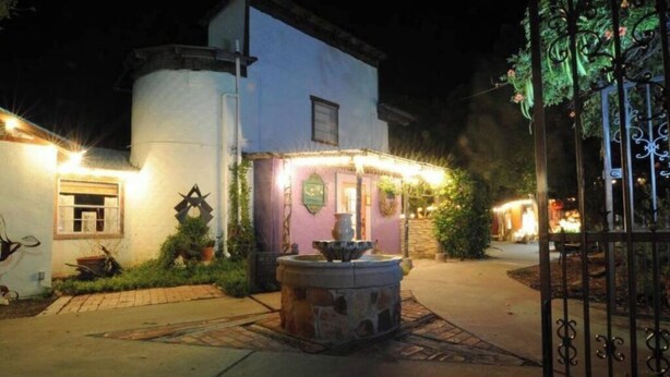 A nighttime view of a building with a fountain in the center, surrounded by greenery and a decorative gate.