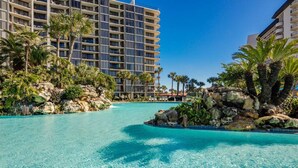 A clear blue pool surrounded by palm trees and a hotel building. - Gulf-View Balcony at Edgewater Resort (Panama City Beach)