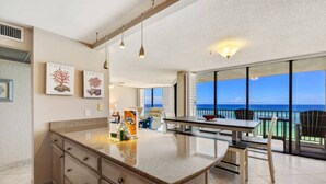A modern kitchen with a large island, a dining area with a view of the ocean, and a balcony with a railing. - Gulf-View Balcony at Edgewater Resort (Panama City Beach)