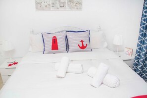 Un lit bien fait, avec des draps blancs, deux oreillers ornés de motifs marins et des serviettes enroulées posées sur le lit.