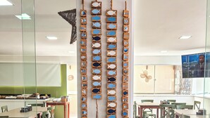 A room with wicker chairs, a table with a glass and rope decoration, and a wall with wooden fish decorations. - Pousada Jardins Tropical (Ipojuca)