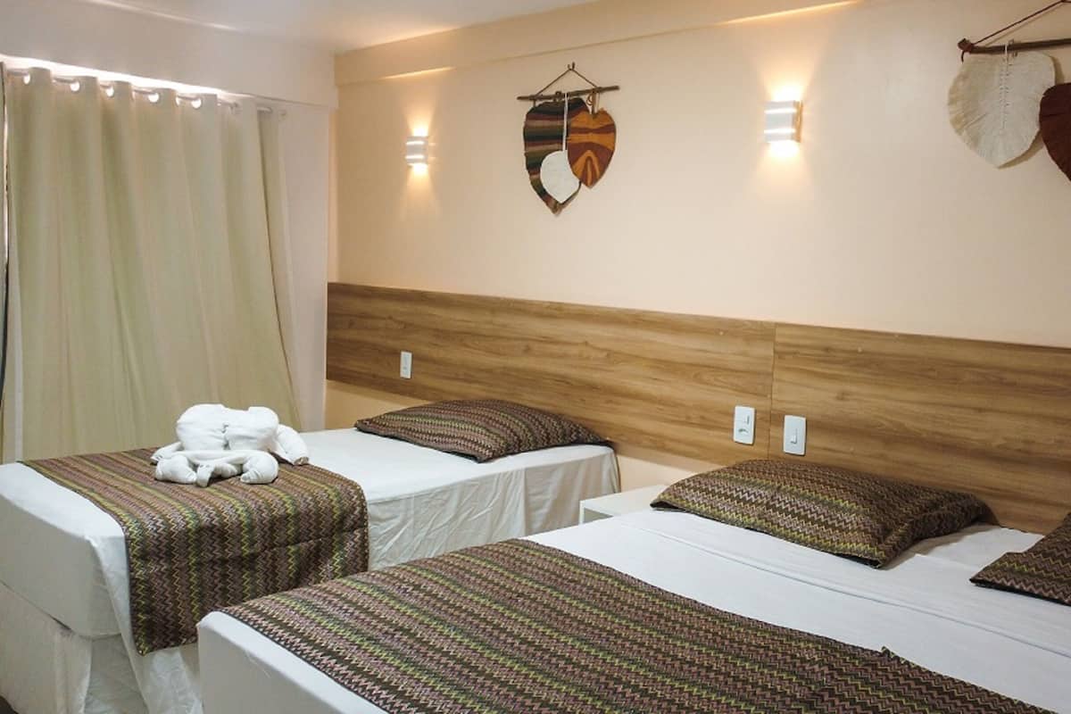 A hotel room with two beds, each with patterned bedding and pillows, a wooden headboard, and wall-mounted light fixtures.