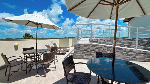 An outdoor patio with tables and chairs, umbrellas, and a view of the landscape. - Pousada Jardins Tropical (Ipojuca)